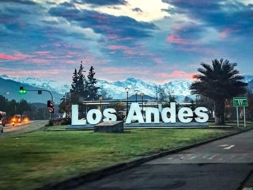 Letrero de bienvenida de la ciudad de Los Andes con la cordillera nevada al fondo durante el atardecer